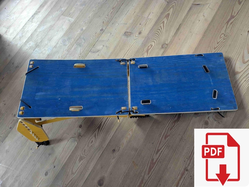 May include: A foldable blue wooden laptop desk with yellow legs. The desk is split into two sections and has several cut-out handles. The desk is designed to be portable and easy to store. The desk is on a wooden floor.