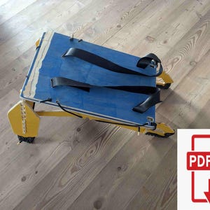 May include: A handmade wooden sled with a blue top and yellow frame. The sled has black straps and is designed for recreational use. The sled's dimensions are approximately 30 inches long and 15 inches wide.