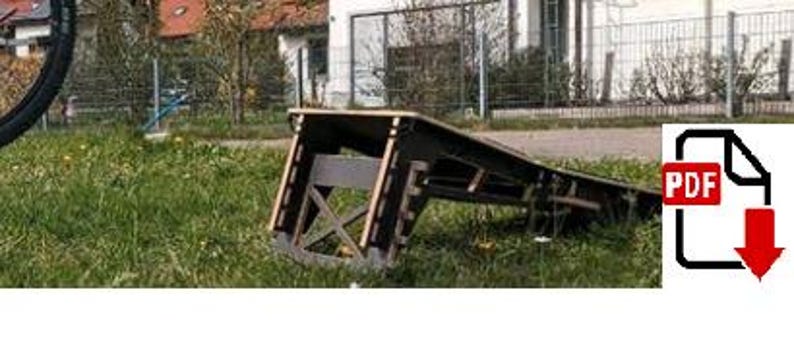 Peut inclure: Une rampe en bois noire et marron pour v&eacute;los sur une pelouse. La rampe a une surface inclin&eacute;e et un cadre de support. Une roue de v&eacute;lo est visible &agrave; gauche. Une ic&ocirc;ne PDF est dans le coin inf&eacute;rieur droit.
