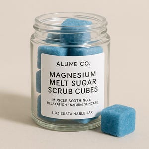 May include: A clear glass jar filled with blue magnesium melt sugar scrub cubes. The jar has a white label with the text "ALUME CO. MAGNESIUM MELT SUGAR SCRUB CUBES". The label also states "MUSCLE SOOTHING & RELAXATION NATURAL SKINCARE" and "4 OZ SUSTAINABLE JAR".