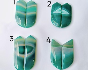 May include: Four pairs of polished, shield-shaped green agate gemstones labeled 1 through 4. Each pair features smooth, translucent surfaces with distinct horizontal and curved white and dark green banding patterns, showcasing a glossy finish.