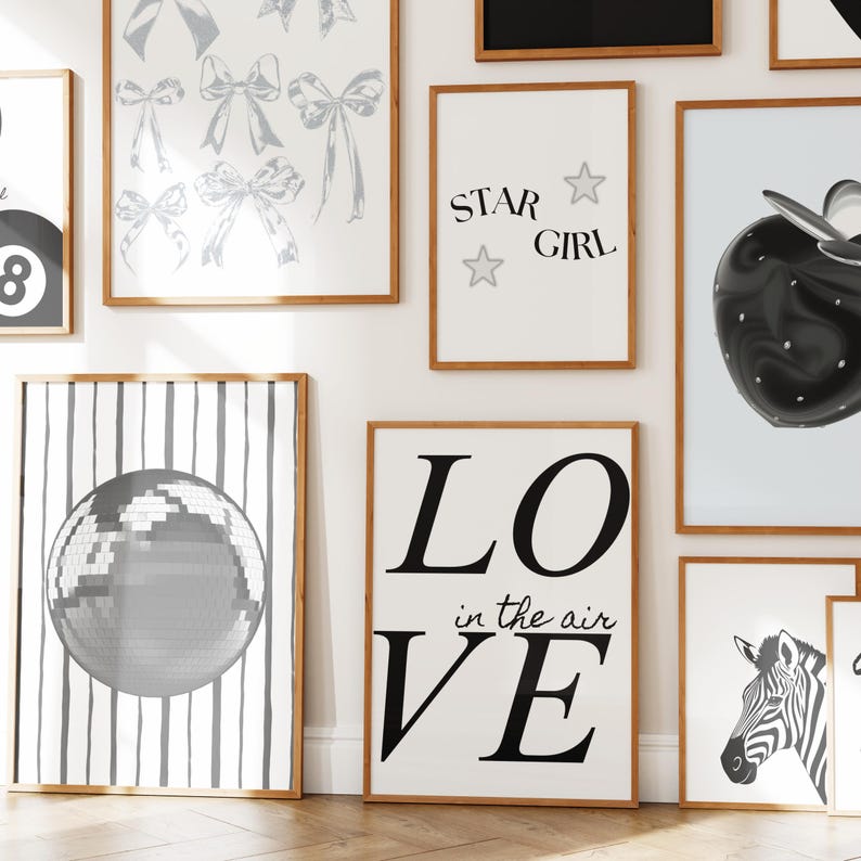 Pu&ograve; includere: Una collezione di stampe artistiche incorniciate con vari disegni. Le stampe includono illustrazioni di fiocchi, il testo "STAR GIRL", una palla da discoteca, il testo "LO in the air VE", una zebra e una mela nera. Le cornici sono di colore marrone chiaro.