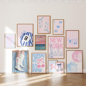 May include: A selection of framed art prints in pink, blue, and white. The prints depict diverse imagery, such as a lucky 8 ball, ballet shoes, a New York City skyline, and a disco ball. The prints are displayed on a white wall.