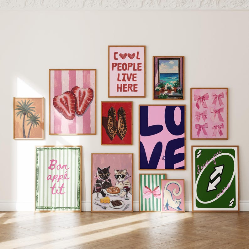 May include: A selection of framed art prints with diverse designs. Includes a pink and white striped print with strawberry halves, a print with the text "COOL PEOPLE LIVE HERE", and a print with the word "LOVE". Other prints feature cats, bows, and a palm tree.