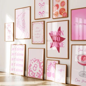 May include: A gallery wall collection of eleven framed art prints featuring pink and white color palettes. Designs include text like 'lucky girl', 'born to shine', 'je t'aime', and 'do it anyway', alongside illustrations of bows, citrus slices, an eight ball, and a cocktail.