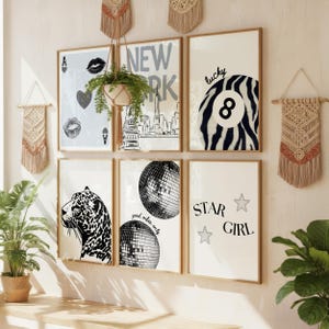 Pu&ograve; includere: Una collezione di stampe artistiche incorniciate con una variet&agrave; di disegni, tra cui uno skyline di New York City, un leopardo, una palla da discoteca e le parole "Star Girl". Le stampe sono in tonalit&agrave; neutre e sono esposte su una parete con decorazioni murali in macram&egrave;.