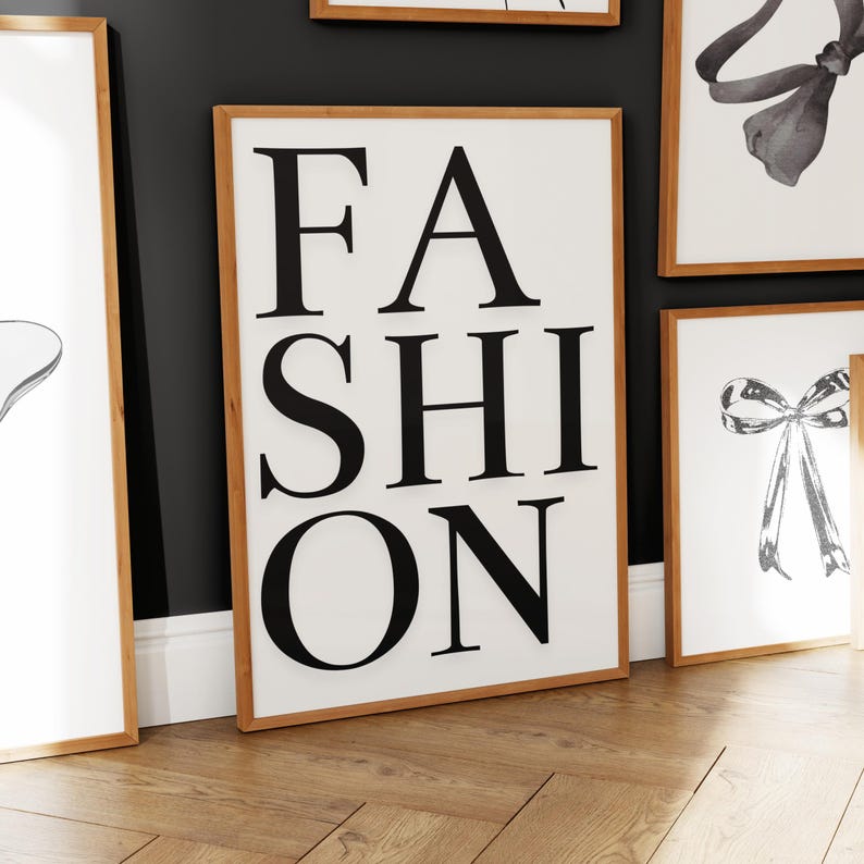 Pu&ograve; includere: Una stampa artistica incorniciata con la parola "FASHION" in grandi lettere nere e in grassetto su sfondo bianco. La cornice &egrave; di colore marrone chiaro. Altre opere d'arte incorniciate sono visibili sullo sfondo.