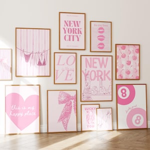 Puede incluir: Una colecci&oacute;n de pared de once l&aacute;minas enmarcadas con esquemas de color rosa y blanco. Los dise&ntilde;os incluyen tipograf&iacute;a de New York City, un bikini en un tendedero, cerezas, un coraz&oacute;n grande con texto, un lazo y bolas de billar n&uacute;mero 8.