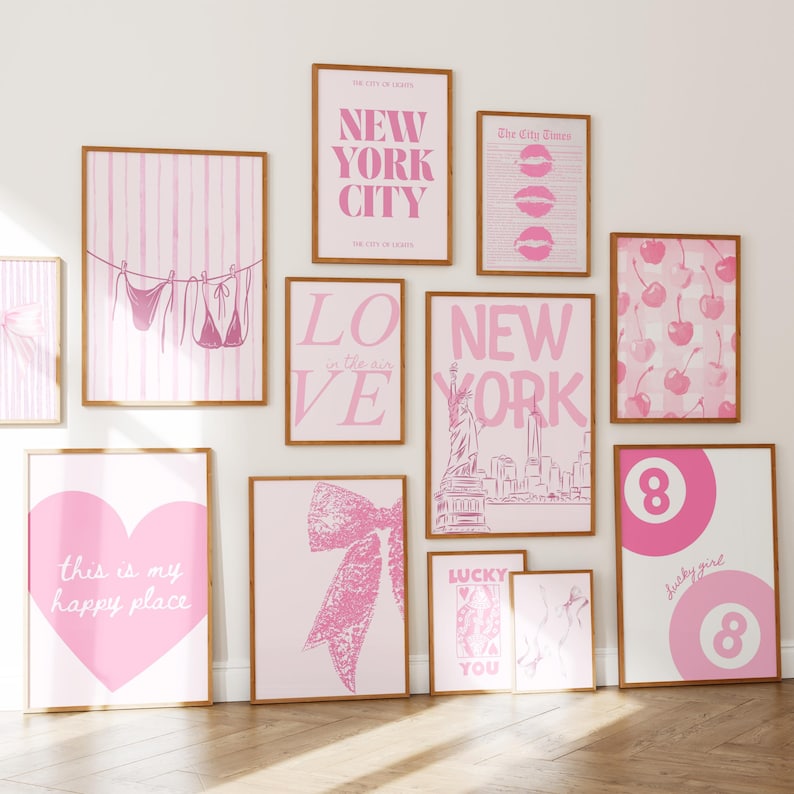 Puede incluir: Una colecci&oacute;n de pared de once l&aacute;minas enmarcadas con esquemas de color rosa y blanco. Los dise&ntilde;os incluyen tipograf&iacute;a de New York City, un bikini en un tendedero, cerezas, un coraz&oacute;n grande con texto, un lazo y bolas de billar n&uacute;mero 8.