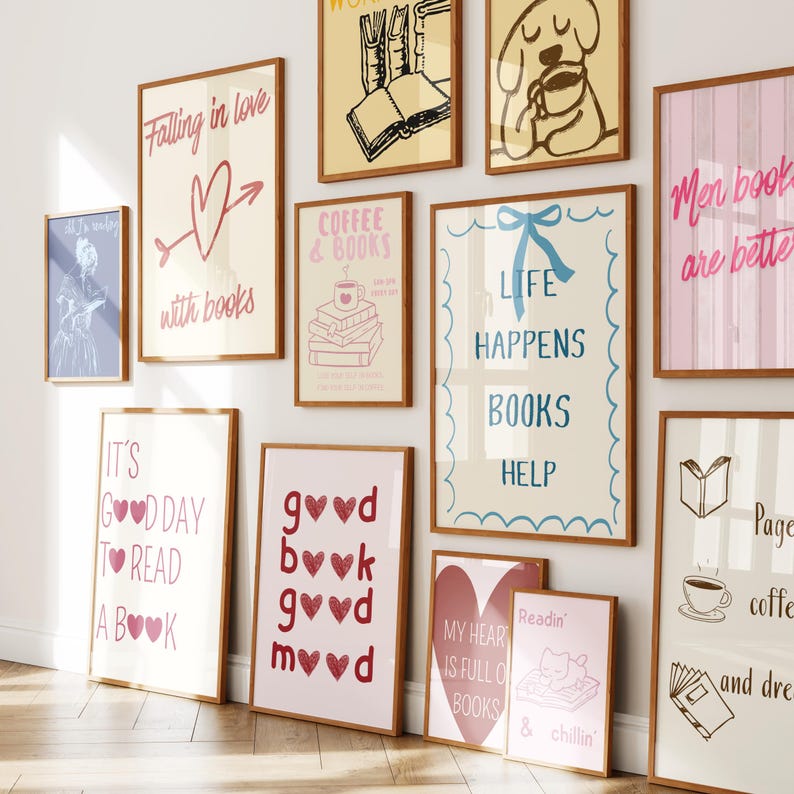 May include: A collection of framed art prints with book-themed designs. The prints feature quotes like "Falling in love with books" and "Life happens, books help." Colors include pink, red, and blue, with wooden frames. The artwork is displayed on a white wall.