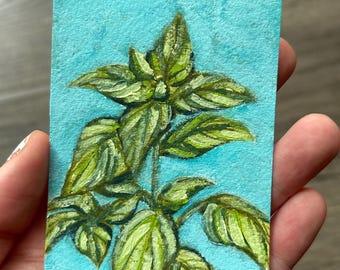 May include: A small rectangular painting on textured paper featuring a green basil plant with detailed leaves against a solid bright turquoise blue background. The artwork displays visible brushstrokes and layered shades of green and yellow.