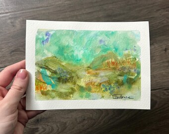 May include: A rectangular watercolor painting on textured white paper featuring an abstract landscape with washes of green, yellow, and blue. The composition includes layered brushstrokes, hints of orange, and a signature reading Isa Grace.