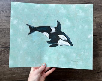 May include: A rectangular art print featuring a painted orca whale in black and white with distinct patches, swimming against a textured, light mint green background. The artwork includes a small, handwritten signature in the bottom right corner.
