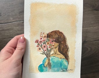 May include: A watercolor painting on textured paper depicting a figure with long brown hair wearing a bright blue off-the-shoulder top. The figure holds a bouquet of small pink and orange flowers in front of their face. The background is a soft peach wash.