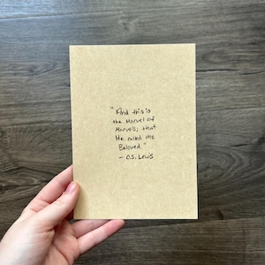 May include: A tan card with handwritten text. The quote reads: "And this is the Marvel of Marvels; that He called me Beloved." - C.S. Lewis. The card is held by a person.