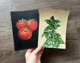 May include: Two rectangular paintings on paper. The left painting features three red tomatoes with green stems against a solid black background. The right painting depicts a green basil plant with detailed leaves against a light beige background.