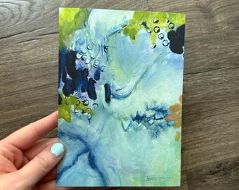 May include: A rectangular art print featuring an abstract composition with layered shades of light blue, lime green, and deep navy. The design includes dark brushstrokes, small circular outlines, and a signature in the bottom right corner.