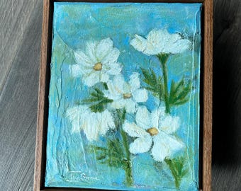 May include: A rectangular canvas painting featuring four white flowers with yellow centres against a textured blue and green background, enclosed in a natural wood frame. The artist signature Isa Grace is visible in the bottom left corner.