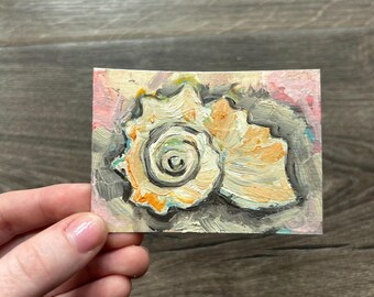 May include: A small rectangular painting featuring an oil-style depiction of a spiral seashell. The shell is rendered in shades of cream, orange, and yellow, set against a textured background of grey, pink, and white brushstrokes with visible paint texture.