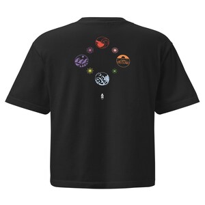 May include: Black t-shirt featuring a circular design on the back with colorful illustrations of waves, mountains, and suns. The design is arranged in a diamond shape. The shirt has short sleeves and a crew neck.