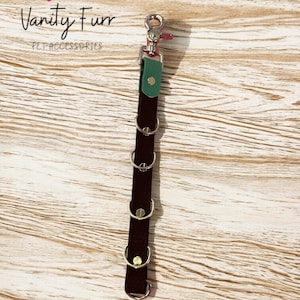 Puede incluir: Un extensor de mesa negro con anillos plateados y un acento verde. El extensor tiene un cierre plateado y está etiquetado como "Table Extender". También es visible la marca "Vanity Furr PET ACCESSORIES".