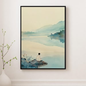 Op de afbeelding: Een ingelijste aquarelprint toont een serene landschap met een persoon die op een rots zit en naar een rustig meer kijkt. Het kunstwerk heeft zachte blauw- en groentinten, met een bergketen op de achtergrond. De print zit in een zwarte lijst.