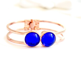 May include: A rose gold bangle bracelet with two blue glass cabochons.