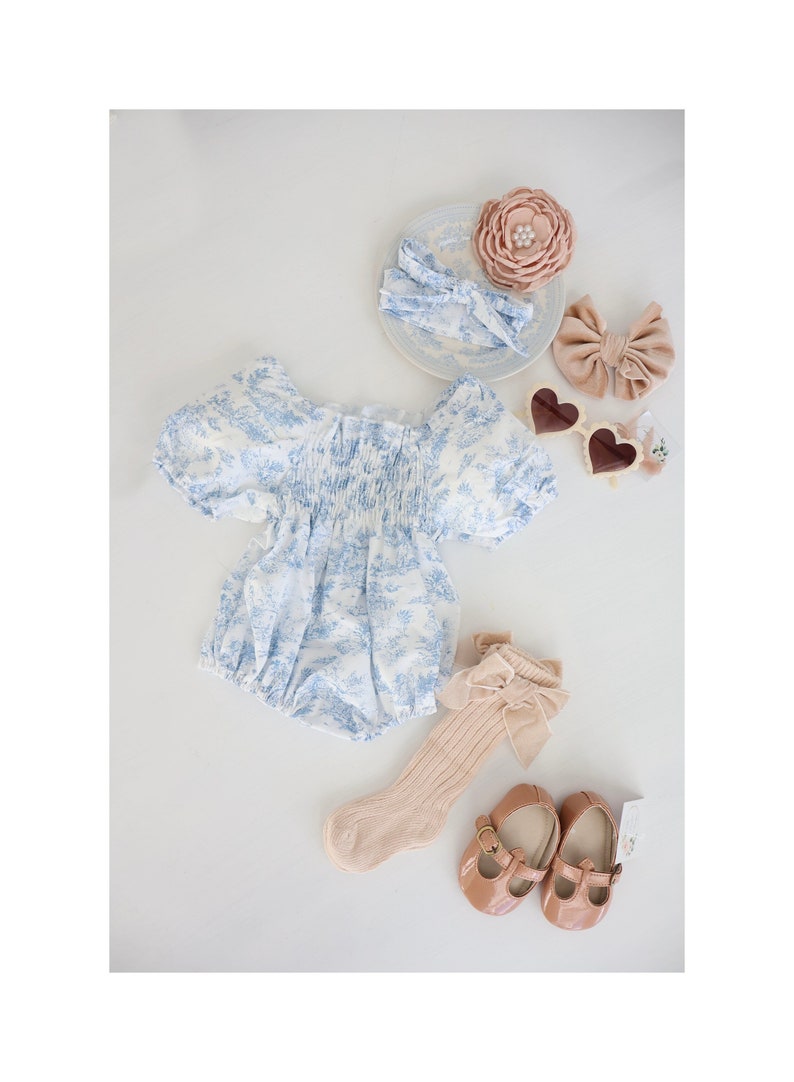 May include: A baby outfit set with a blue and white floral print romper, a pair of beige socks with a bow, a pair of brown leather shoes, and two hair bows in pink and brown.