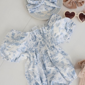 May include: A white and blue floral print baby onesie with puffed sleeves and a gathered elastic waistband.