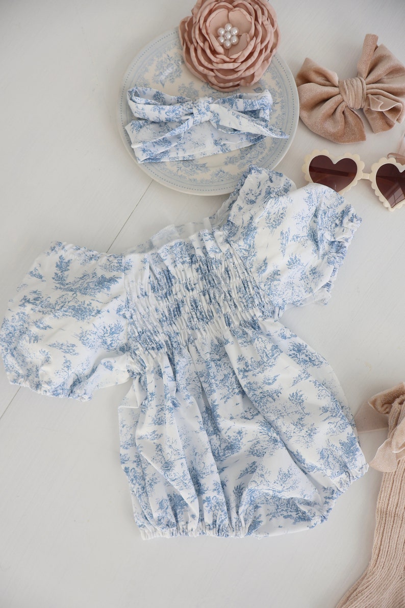 May include: A white and blue floral print baby onesie with puffed sleeves and a gathered elastic waistband.