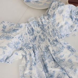 May include: A white dress with a blue floral pattern. The dress has a gathered bodice and short sleeves.
