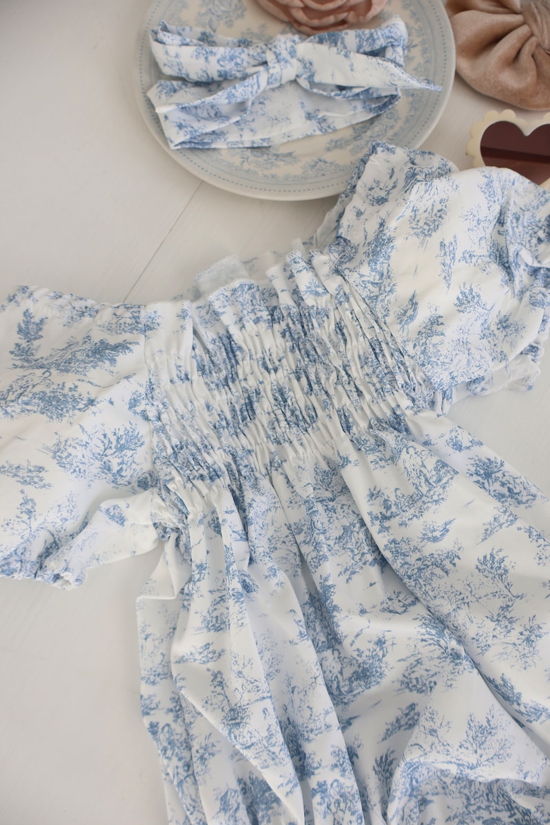 May include: A white dress with a blue floral pattern. The dress has a gathered bodice and short sleeves.