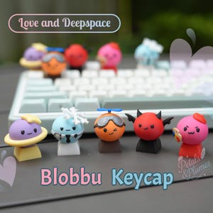 Peut inclure: Ensemble de touches de clavier colorées de style dessin animé, chacune avec un design unique. Les touches présentent des personnages avec divers accessoires, dont un diable, un pilote et une figurine sur le thème de l'espace. Le texte "Blobbu Keycap" est affiché en bas.