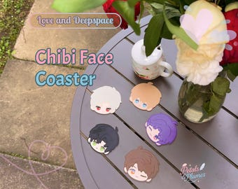 May include: A collection of Chibi Face coasters in various colors, featuring anime-style character designs. The coasters are arranged on a gray table, alongside a floral arrangement and a small mug. The text "Chibi Face Coaster" is visible.