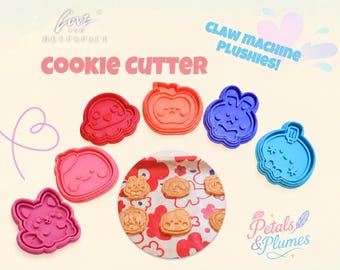 May include: A set of six plastic cookie cutters in various colors including red, pink, blue, and magenta, featuring character shapes. The image includes text reading LOVE AND DEEPSPACE, COOKIE CUTTER, CLAW MACHINE PLUSHIES!, and Petals & Plumes.