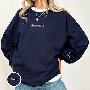 以下が含まれることがあります： 白襟と胸元の小さなキラキラデザインが特徴のネイビーブルーのスウェットシャツ。「Emily」の文字が袖に刺繍されています。ゆったりとしたフィット感のスウェットシャツです。