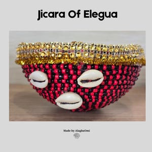 Pode incluir: Uma tigela Jicara Of Elegua decorada com um padrão de contas pretas e vermelhas alternadas. A borda apresenta um acabamento metálico dourado e três conchas de búzios brancas estão fixadas no exterior. O texto diz Jicara Of Elegua.