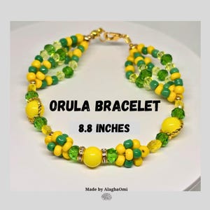 May include: A beaded bracelet with the text "ORULA BRACELET" and "8.8 INCHES". The bracelet features yellow, green, and gold beads. The bracelet is made with multiple strands and has a gold clasp. The bracelet is on a white surface.