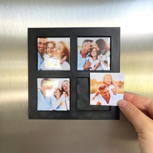 Peut inclure: Cadre photo magn&eacute;tique noir avec quatre ouvertures carr&eacute;es, chacune contenant une photo de famille. Une photo est tenue par une main. Le cadre est fix&eacute; &agrave; une porte de r&eacute;frig&eacute;rateur argent&eacute;e. Les photos montrent des familles heureuses.
