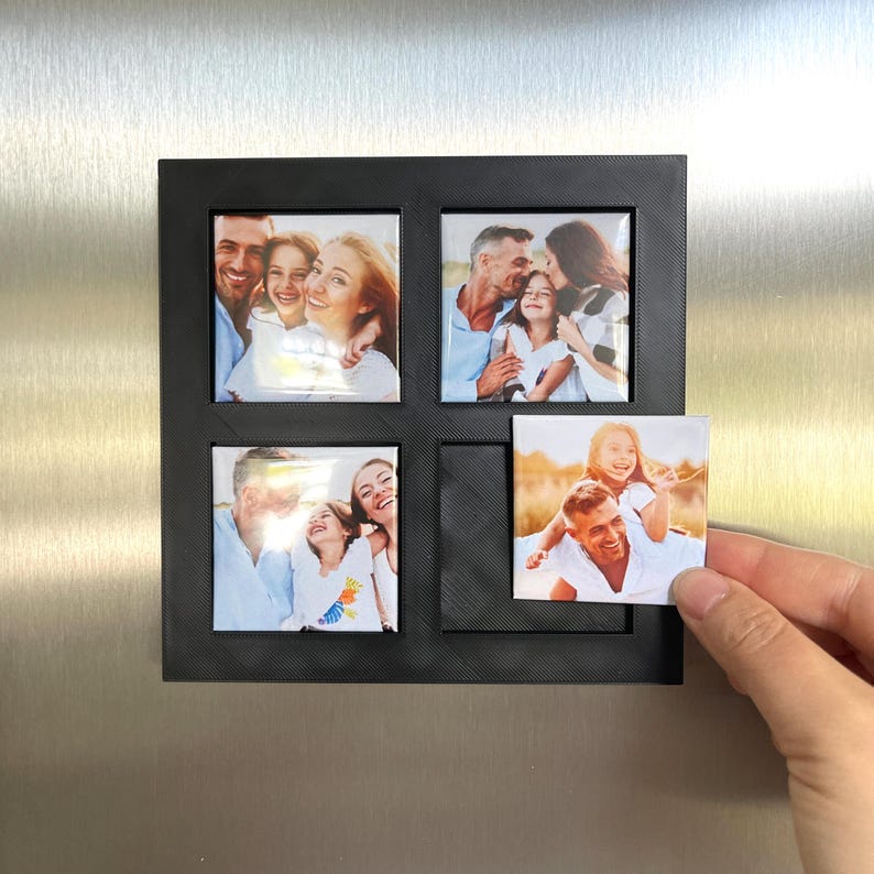 Peut inclure: Cadre photo magn&eacute;tique noir avec quatre ouvertures carr&eacute;es, chacune contenant une photo de famille. Une photo est tenue par une main. Le cadre est fix&eacute; &agrave; une porte de r&eacute;frig&eacute;rateur argent&eacute;e. Les photos montrent des familles heureuses.
