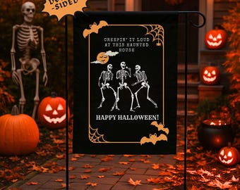 以下が含まれることがあります： 黒い背景とオレンジ色のアクセントが施された、両面ハロウィーンガーデンフラッグ。 フラッグには、骸骨、コウモリ、テキスト「CREEPIN' IT LOUD AT THIS HAUNTED HOUSE」と「HAPPY HALLOWEEN！」のデザインが施されています。 フラッグは、ライトアップされたカボチャとともに屋外に表示されています。
