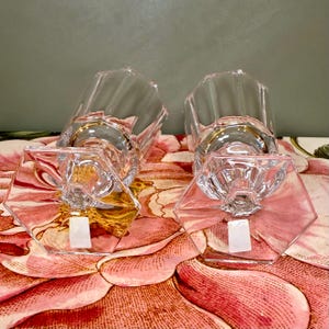 K&ouml;nnte beinhalten: Zwei klare, facettierte Glas-Kerzenhalter mit goldenen R&auml;ndern. Die Basen sind sechseckig. Die Kerzenhalter stehen auf einer Oberfl&auml;che mit Blumenmuster mit rosa und roten Blumen.