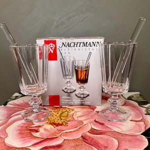 K&ouml;nnte beinhalten: Klare Kristall-Grog-Gl&auml;ser mit R&uuml;hrst&auml;bchen. Die Gl&auml;ser haben ein facettiertes Design und stehen auf einem dekorativen Sockel. Eine Schachtel mit Nachtmann Kristall-Grog-Gl&auml;sern befindet sich hinter den Gl&auml;sern.