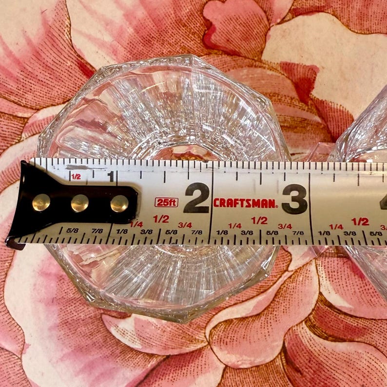 K&ouml;nnte beinhalten: Klarer, achteckiger Glasuntersetzer mit geripptem Design. Der Untersetzer hat einen Durchmesser von ca. 6,35 cm. Der Untersetzer befindet sich auf einem floral gemusterten Hintergrund.