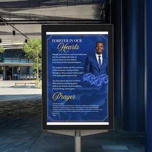 May include: A memorial sign with the words "FOREVER IN OUR Hearts" in elegant script. The sign features a photo of a man in a suit, surrounded by blue roses and a poem. The word "Prayer" is also displayed.