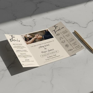 Puede incluir: Una invitaci&oacute;n de boda tr&iacute;ptica de color crema con una foto de una pareja. La invitaci&oacute;n incluye los nombres Amy Ioius y Peter James, y una l&iacute;nea de tiempo. Un bol&iacute;grafo dorado descansa cerca.