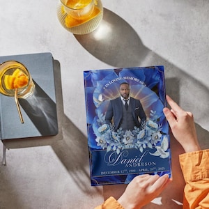 May include: A memorial print featuring a portrait of a man in a suit, set against a backdrop of blue floral designs. The print includes the text "In Loving Memory Of", the name "Daniel Andreson", and the dates "December 12th, 1900 - April 20th, 2025".