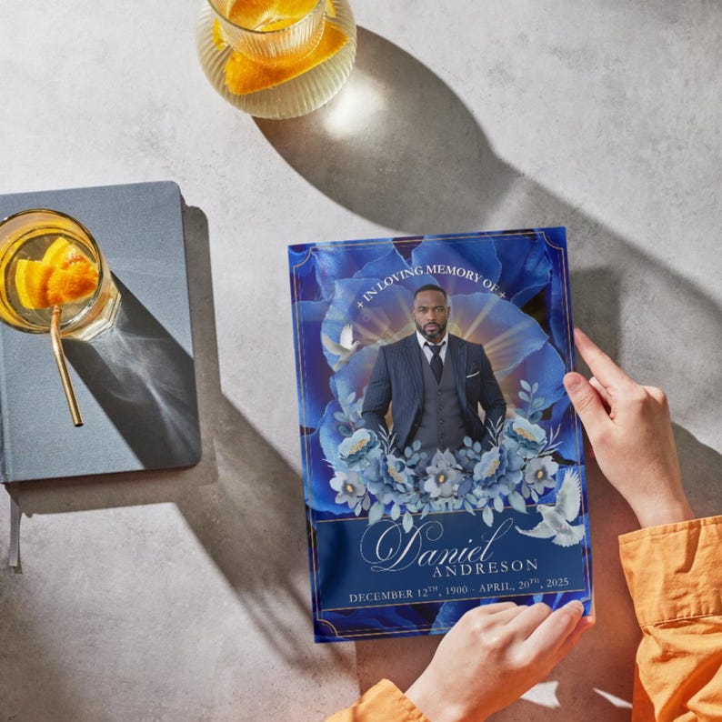May include: A memorial print featuring a portrait of a man in a suit, set against a backdrop of blue floral designs. The print includes the text "In Loving Memory Of", the name "Daniel Andreson", and the dates "December 12th, 1900 - April 20th, 2025".
