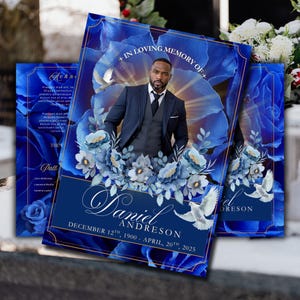 May include: A memorial card with a portrait of a man in a suit, set against a backdrop of blue floral elements and doves. The card displays the text "+ IN LOVING MEMORY OF +" and the name "Daniel Andreson" with dates. The design is predominantly deep blue with gold detailing.