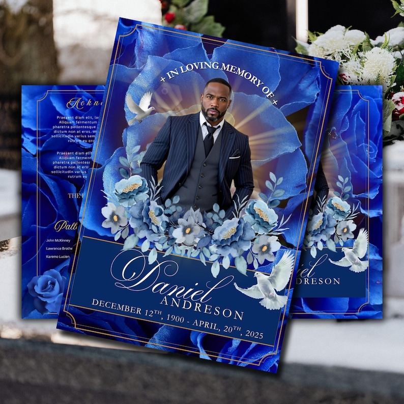 May include: A memorial card with a portrait of a man in a suit, set against a backdrop of blue floral elements and doves. The card displays the text "+ IN LOVING MEMORY OF +" and the name "Daniel Andreson" with dates. The design is predominantly deep blue with gold detailing.